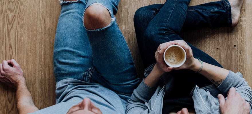Paar liegt auf Parkettboden und trinkt Kaffee